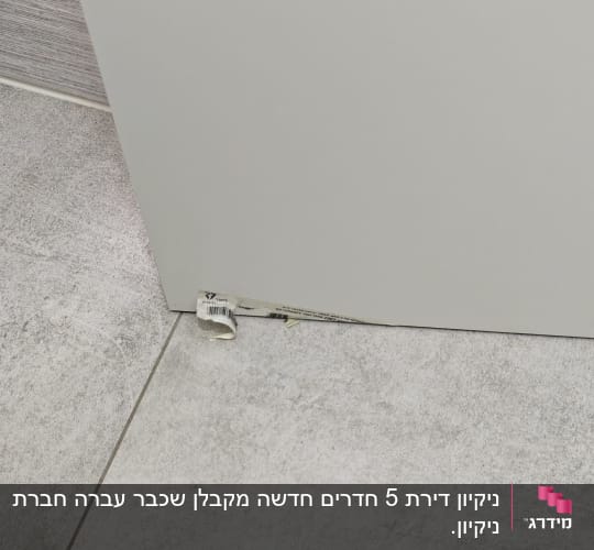 תקריב של תחתית דלת עם מדבקה חצי מקולפת על ריצוף אפור